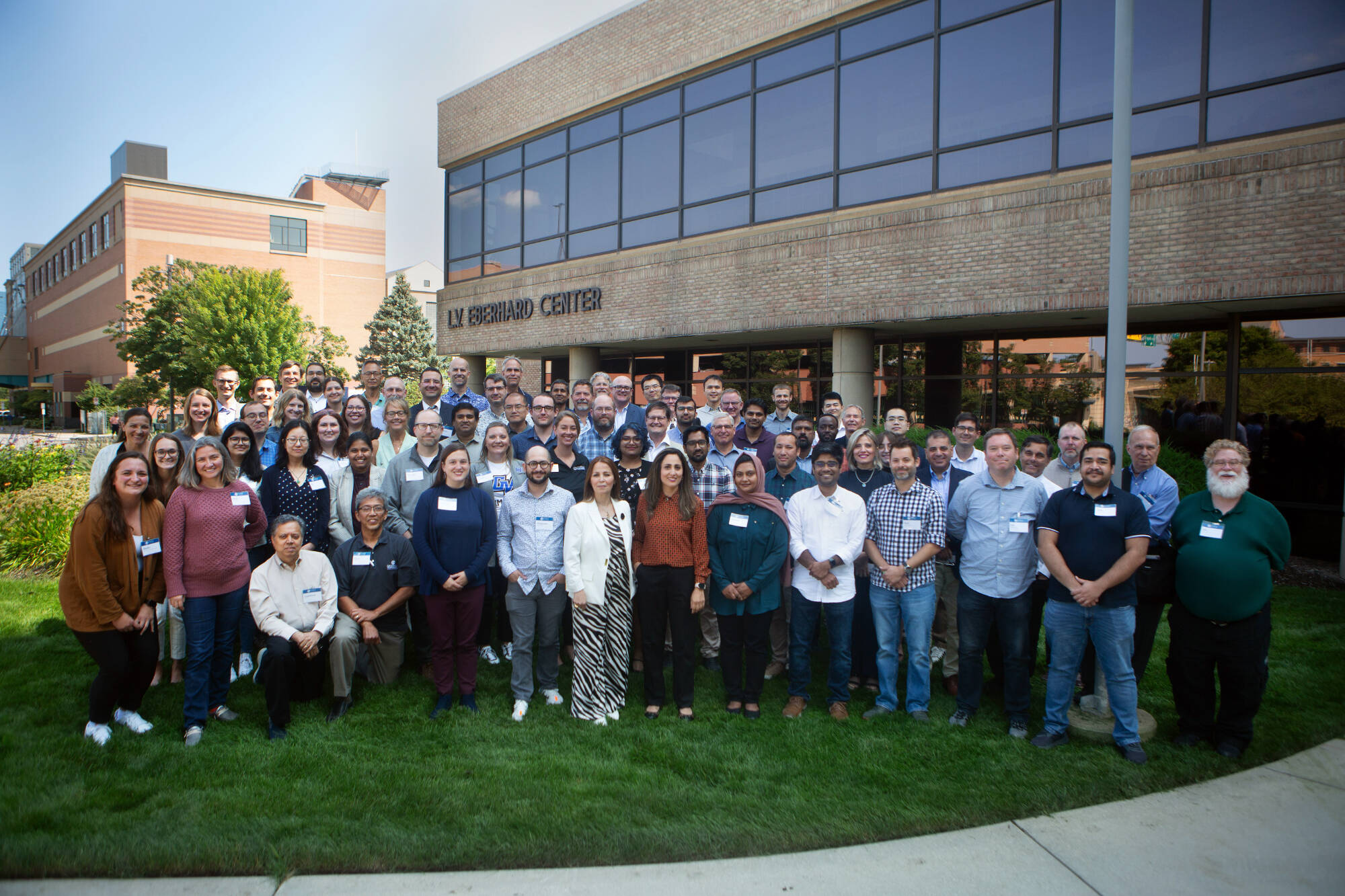 Group photo of College of Computing faculty and staff at Grand Valley State University standing outside the L.V. Eberhard Center. The diverse group is smiling and gathered on a grassy area in front of the building, representing the full team of educators,